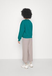 Teal oversized sweatshirt med rund halsringning, tillsammans med ljusgrå vida byxor och vita sneakers. Casual, mjukt tyg.