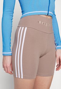 Bruna shorts med vita sidosträck och hög midja med en logotyp i ljus text. Tillverkade av stretchigt tyg med en mjuk textur.