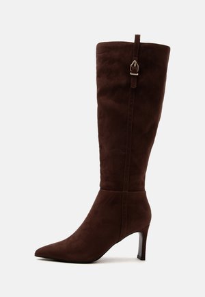 Botte haute en daim marron foncé avec bout pointu, talon fin et haut, et une sangle décorative à boucle en métal sur la tige.