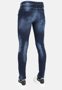 Donkerblauwe jeans met een slim fit, met een vervaagde textuur, vijf zakken en details op de achterste yoke, gecombineerd met wit en zwarte sneakers.
