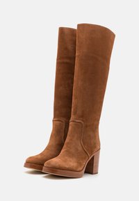 Marron suède botte haut jusqu'au genou avec un talon rectangulaire, bout rond et couture décorative le long de la couture.