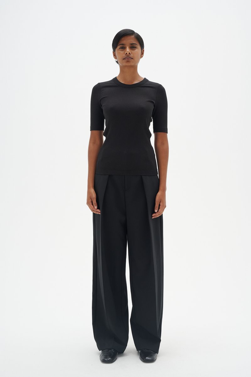 Melnas ribotas īsām piedurknēm blūze, kas savienota ar augstiem melniem plats kāju biksēm. Gluda tekstūra, pielāgota piegriezuma un minimālistisks dizains.