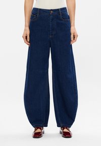 Παντελόνι από μπλε τζιν με φαρδιά πόδια, διαθέτει υψηλή μέση, μπροστινές τσέπες και ραφές. Το ύφασμα έχει λεία υφή και χαλαρή εμφάνιση.