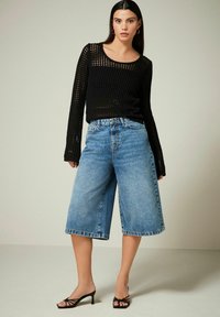 Maglione nero lavorato a maglia con maniche lunghe, abbinato a culotte in denim azzurro chiaro. Tacchi neri open-toe completano l'outfit.
