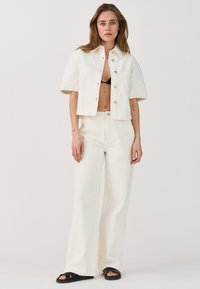 Completo a due pezzi in tessuto bianco testurizzato; camicia corta a maniche corte con bottoni e pantaloni a vita alta a gamba larga coordinati. Sandali neri.