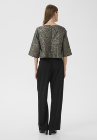 Jachetă scurtă, texturată, în nuanțe de verde închis și auriu, cu mâneci largi și decolteu pătrat pe spate, asortată cu pantaloni negri cu talie înaltă.