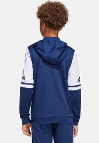 Marineblauwe hoodie met witte mouwen, voorzien van een trekkoord in de capuchon en geborduurde drie strepen op de schouders. Soepele, lichtgewicht stof.