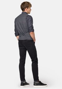 Szary kamizelka w kratę na ciemnej koszuli, czarne dopasowane spodnie i czarne teksturowane trampki. Kamizelka ma możliwość regulacji w talii.