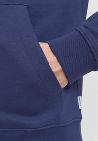 Marineblå sweatshirt med en frontlomme og ribbede manchetter. Fremstillet af blødt stof med flade sømme og et mærke på siden.