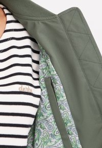 Grön jacka med quiltat mönster och randig svart-vit skjorta under. Fodret har en indviket grön paisleymönster.