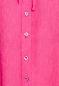 Camicia rosa con texture, dotata di apertura con bottoni e sei bottoni silver. Dettaglio con coulisse sul collo.