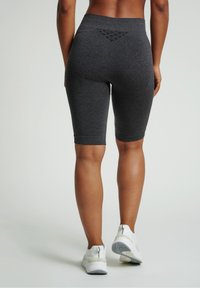 Vysoké šedé cyklistické šortky s texturovanou zadní stranou a žebrovanými manžetami, spárované s bílými sportovními botami s detailem na zip.