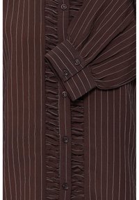 Blouse marron à manches longues avec fines rayures blanches verticales, poignets boutonnés et volants le long de la patte de boutonnage devant.