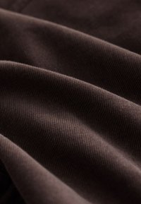 Brązowa tkanina o prążkowanej fakturze, z miękkimi, płynnymi fałdami i subtelnym połyskiem; odpowiednia do różnych zastosowań tekstylnych.