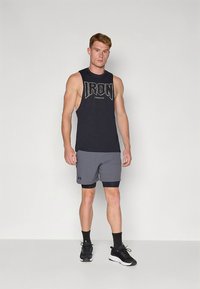 Camisola desportiva preta sem mangas com estampagem "IRON", combinada com calções cinza com cintura preta. Usada com sapatilhas desportivas pretas.