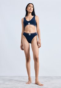 Navy blue bra and bikini set with a sporty design, featuring a logo patch and contrasting red and white stripes along the bands.