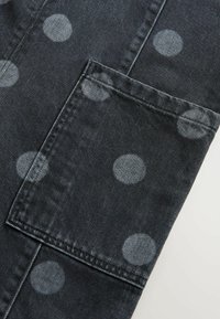 Tela de mezclilla con un fondo oscuro y grandes puntos de color gris claro. Presenta un bolsillo tipo parche con costuras visibles y una textura suave.