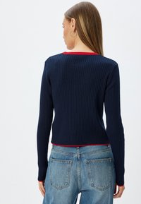 Pullover a coste blu navy con maniche lunghe, taglio corto e dettagli rossi sul collo e sull'orlo. Design casual, texture morbida, silhouette aderente.
