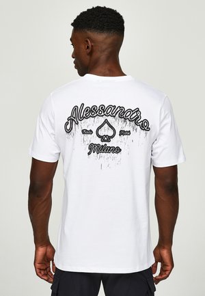Man met kort haar die een wit t-shirt draagt met zwarte "Alessandro Milano" tekst en een schoppenlogo op de rug, staand tegen een effen achtergrond.