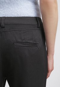 Pantaloni neri con una tasca posteriore a apertura dritta, cuciture a punto e una texture liscia. La vita è piatta e aderente.
