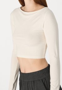 Top corto de manga larga en tejido beige claro, con escote redondo y diseño ajustado, combinado con pantalones de cintura elástica en gris oscuro.