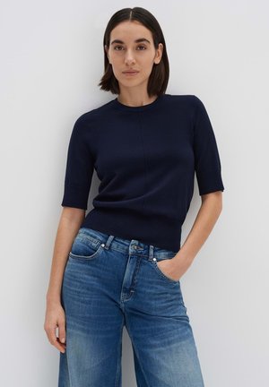 Navyblauer Kurzarmpullover mit Rundhalsausschnitt, der einen figurbetonten Schnitt und eine weiche Textur aufweist, kombiniert mit hellblauen, weiten Jeans.