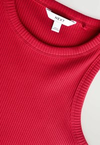 Rotes geripptes Tanktop mit rundem Ausschnitt, das ein strukturiertes Muster zeigt und ein Etikett mit der Marke "NEXT" trägt, hergestellt in Bangladesch.