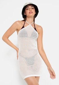 Bílý síťový halter šaty s geometrickým vzorem a přiléhavým střihem. Zdobené tmavě hnědým výstřihem a nastavitelnými tkanicemi.