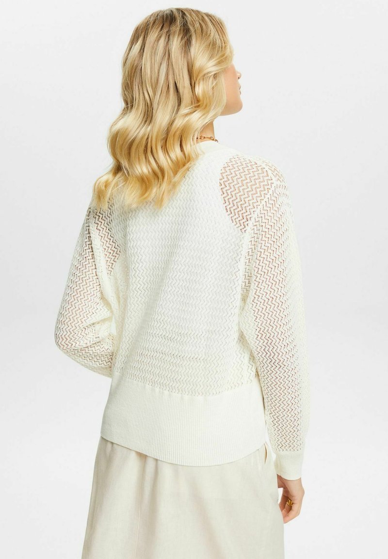 Pull en tricot blanc avec un motif texturé, présentant des détails en maille ouverte aux manches et dans le haut du dos, ainsi qu'un ourlet côtelé.