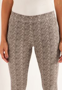 Leggings gris à motifs avec une surface texturée, dotés d'une taille élastique et d'une coupe ajustée. Des poches sont visibles sur les côtés.
