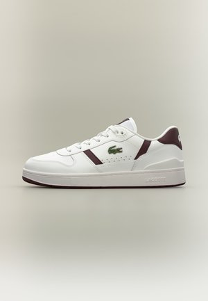 Baskets basses Lacoste blanches et bordeaux avec lacets, logo crocodile vert sur le côté et semelle épaisse sur fond uni.