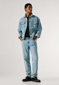 Světlá džínová bunda se dvěma kapsami na hrudi, pod ní černé tričko, středně modré džíny a černé šněrovací boty. Jednoduchý design, volný střih.