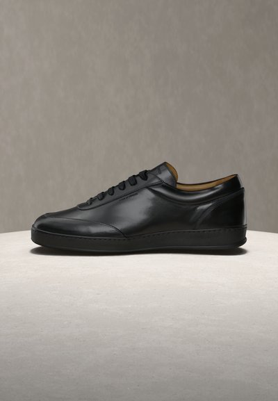 Μαύρο δερμάτινο αθλητικό παπούτσι χαμηλού ύψους με μαύρα κορδόνια, λείο φινίρισμα και επενδυμένο κολάρο, παρουσιασμένο σε ανοιχτή επιφάνεια με ουδέτερο φόντο.