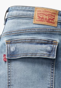 Jeans de mezclilla azul claro con un bolsillo plano y una etiqueta roja de Levi's. Presenta una etiqueta de cuero marrón con un logo en relieve y detalles de costura.