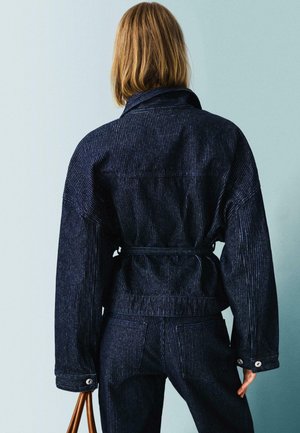 Donkerblauwe denimjack met verticale strepen, een ceintuur in de taille, oversized pasvorm en gestructureerde stof. Voorzien van knoopmanchetten en achterzakken.
