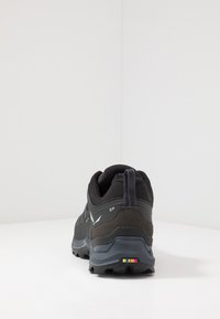 Pantofi de drumeție negri, cu materiale din plasă și piele velur, talpă robustă, tab de tragere la călcâi, accente reflective și o dâră colorată pe spate.