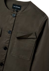 Camisa de botones en verde oliva oscuro con cuello redondo, botones negros y un bolsillo cuadrado en el pecho con solapa en el lado derecho.