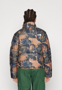 Brun och marinblå puffjacka med marmorering, med hög krage, dragkedjestängning och The North Face-logotyp på baksidan.