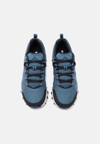 Ζευγάρι μπλε και μαύρα παπούτσια για τρέξιμο σε μονοπάτια Columbia με μαύρα κορδόνια και θηλιές έλξης, εμφανιζόμενα από την επάνω όψη σε λευκό φόντο.