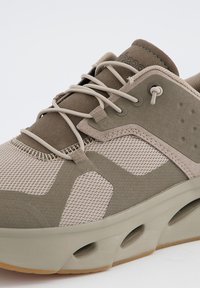 Beige Sport Schuh aus Mesh und Wildledermaterialien, mit strukturierten Akzenten, elastischen Schnürsenkeln und einer dicken, gepolsterten Sohle mit Belüftungsöffnungen.