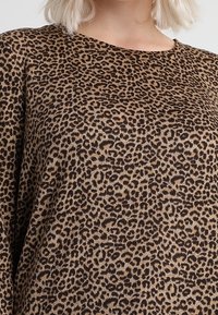 Haut imprimé léopard en marron et beige, avec une coupe ample et une texture douce. Le motif comporte des taches irrégulières sur tout le tissu.