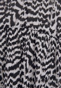 Schwarz-weißer Stoff mit einem markanten, abstrakten Tierdruckdesign, das unterschiedliche wellenförmige Muster und eine weiche, strukturierte Oberfläche aufweist.