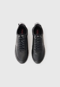 Black athletic shoes with a smooth synthetic upper, lace-up design, padded tongue, and textured accents. Logo printed on the heel and insole.
