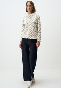 Crème trui met beige zebra-strepen, ronde halslijn en lange mouwen, gecombineerd met wijde donkere denim jeans en witte sneakers.