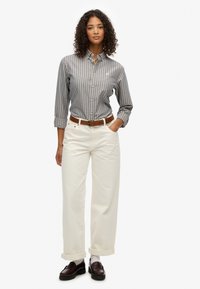 Koszula w paski w odcieniach niebieskiego i beżowego, połączona z wysokim, białym spodniami o szerokich nogawkach. Posiada brązowy pasek i ciemne mokasyny.