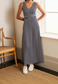 Marinblå och vit randig maxiklänning med V-ringning, figursydd bodice och rynkad midja, i kombination med vita sneakers. Vevstol i bakgrunden.