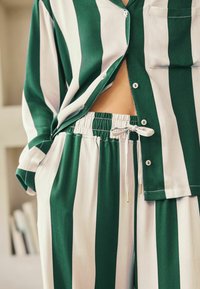 Pyjama rayé vert et blanc comprenant une chemise à boutons avec poche et un pantalon à taille élastique avec cordon de serrage. Tissu doux et coupe décontractée.