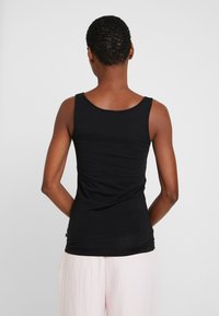 Musta hihaton paita, joka on valmistettu pehmeästä, venyvästä kankaasta. Siinä on pyöreä pääntie ja slim fit -leikkaus. Yhdistetty vaaleanpunaisiin löysiin housuihin.