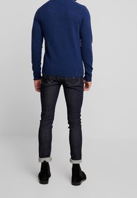 Navy blue knitted sweater with long sleeves and ribbed hem, paired with dark denim jeans and black ankle boots.