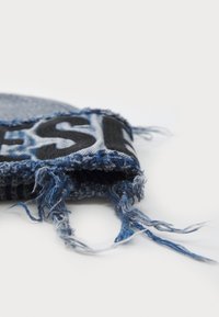 Farmeranyagú termék, rojtos szélekkel, elsősorban kék árnyalatokban, fekete felirattal. Texturált felület, különböző anyagok keverékével.